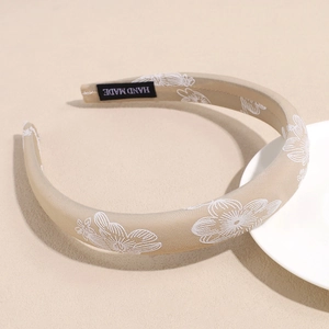 Light brown satin floral embroidered headband with handmade label on beige background