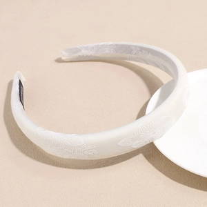 Detailed close-up of cream satin headband with white floral embroidery and sponge padding