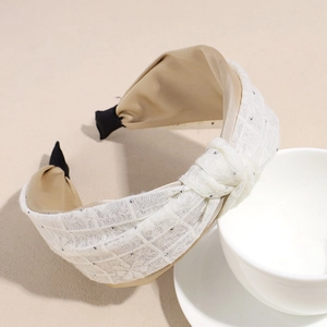 Detail of beige lace headband with floral embroidery and silver beads on a white bowl
