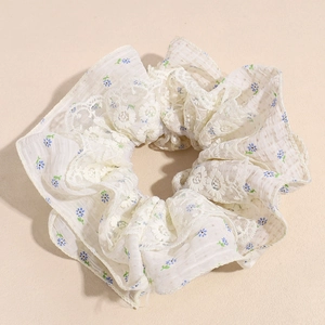 Gros plan sur un chouchou en dentelle blanche avec motif floral bleu et bords ondulés