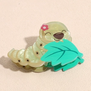 Detailed view of a green cartoon caterpillar hair claw clip with leaf and flower accents