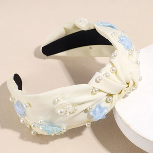 Close-up of cream fabric knotted headband with white pearls and blue starfish charms