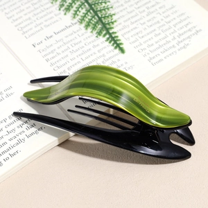 Détail de la barrette vert émeraude avec logo doré sur fond de livre ouvert