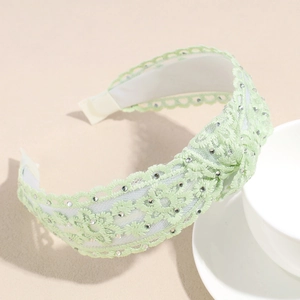Détail macro d'un serre-tête en dentelle vert clair avec strass étincelants et nœud