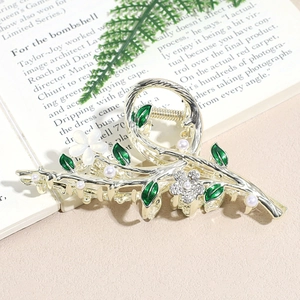 Pince à cheveux fleur argentée avec feuilles vertes et perles sur un livre