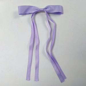 Detail view of light purple satin bow hair clip with long ribbons on white background