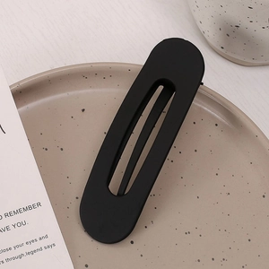Fermaglio ovale nero opaco con design a incastro su un vassoio in ceramica beige