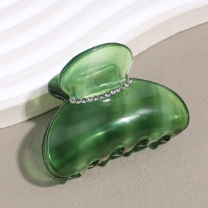 Detailed close-up of green acetate hair claw clip with sparkling rhinestone embellishments