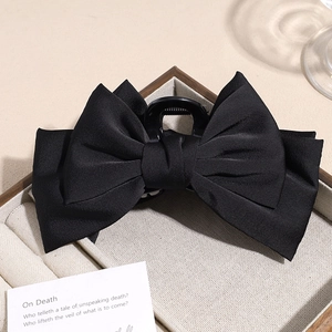 Close-up of a premium black satin double-layered bow hair claw clip on a beige velvet tray