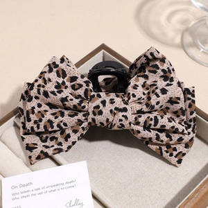 Close-up of leopard print bow hair claw clip displayed on a wooden jewelry tray