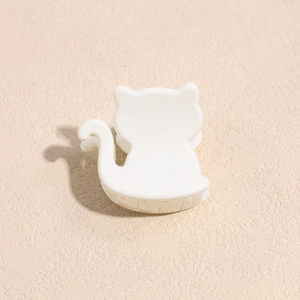 Detailed view of a white acrylic cat-shaped hair claw clip on a textured beige surface