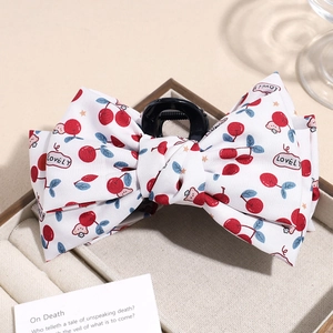 Detail view of large bow hair claw clip with cherry and star pattern in soft light