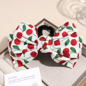 Detail of white fabric bow hair claw with red cherry print in a plush jewelry box