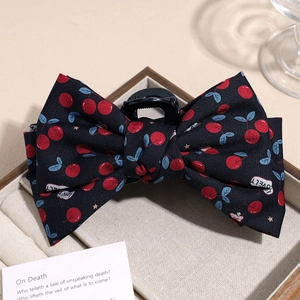 Close-up of fabric bow hair claw clip with vintage cherry pattern on wooden display tray