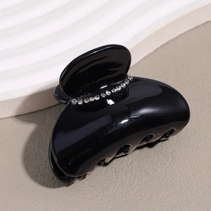 Detailed close-up of glossy black hair claw clip with sparkling rhinestones on top