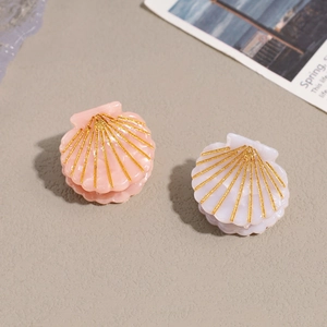 Mini shell-shaped acetate hair clips in pink and white with golden glitter patterns