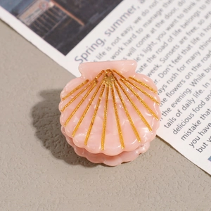 Close-up of shell-shaped pink hair clip with gold glitter details on neutral background