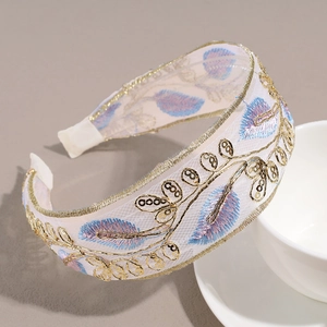 Detail of wide headband featuring gold leaf embroidery and sequins on white mesh fabric