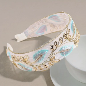 Detailed embroidery on white mesh headband with golden vine sequins and green leaf accents