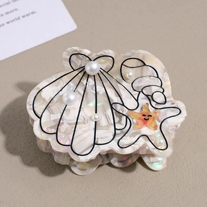 Détail d'une pince à cheveux coquillage avec étoiles et perles sur fond texturé chaud