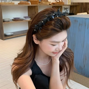 Elegant black bow headband with rhinestones worn by a model in a cozy indoor setting