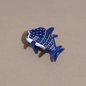 Détail de la pince à cheveux en acétate bleu en forme de requin aux motifs blancs