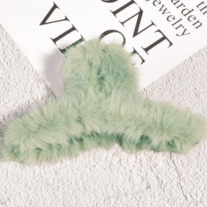 Détail d'une pince à cheveux en peluche vert menthe sur un fond mural blanc texturé
