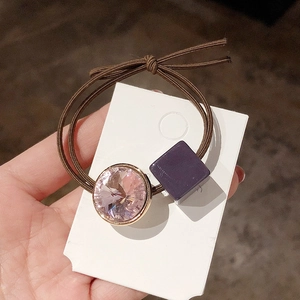 Detailed close-up of elastic hair tie with pink crystal and purple square bead