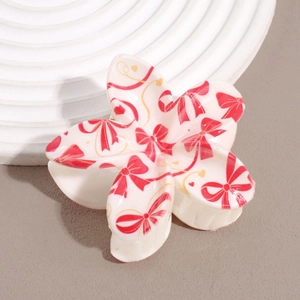 Gros plan d'une pince à cheveux fleurie avec motifs nœuds rouges et fini crème