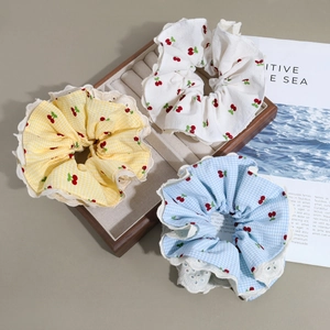 Detailed view of three cherry print scrunchies with lace trim and plaid cotton fabric