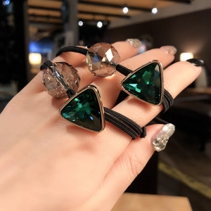 Close-up of elastic hair ties with emerald green and champagne crystal charms on wrist