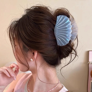 Elegant shell-shaped hair claw with iridescent blue finish on a model's low bun hairstyle
