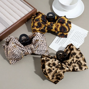 Three elegant leopard print bow hair claws with gold silk threads on a white dish