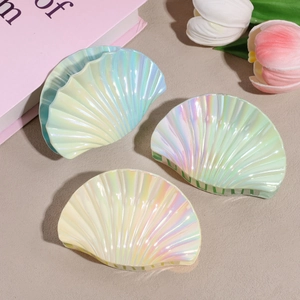 Three colorful iridescent seashell hair claws on a textured stone surface with tulips