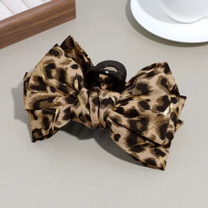 Detail of a leopard print bow hair claw with gold metallic thread in a French style setting