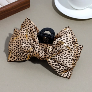 Detail of leopard print bow hair claw with gold foil accents on a minimalist background
