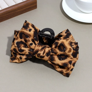 Detail of leopard print bow hair claw clip with rhinestones on a warm-toned background
