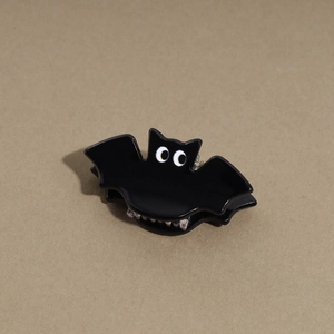 Close-up of a glossy black bat-shaped hair claw clip with large cartoon eyes