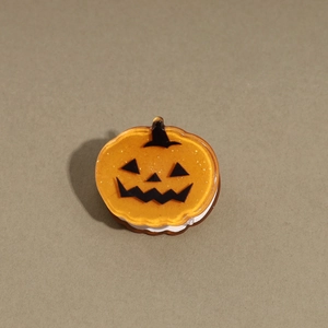 Close-up of a translucent orange pumpkin hair clip with a black Jack-o'-lantern face