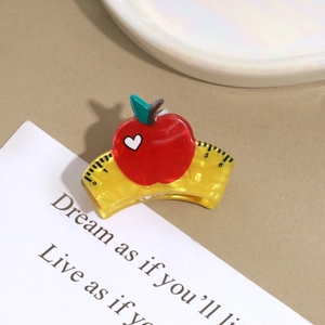 Detail shot of red apple acrylic hair claw clip with yellow ruler scale on warm background