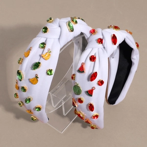 White knotted fabric headband with rhinestones and fruit metal charms on a stand