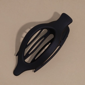 Detailed view of an oval matte black hair claw clip on a minimal sand background