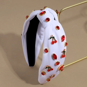 Detail of white knotted headband with red rhinestones and cherry charms on a gold stand
