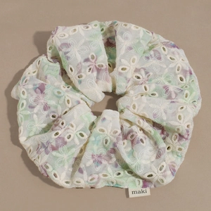 Detailaufnahme des weißen Lochspitze-Haargummis mit floraler Stickerei und Label