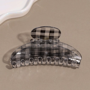 Close-up of a stylish black and white checkered hair claw clip on a beige surface