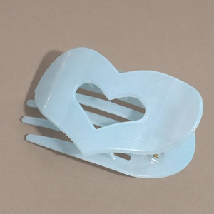 Dettaglio della molletta per capelli a cuore azzurro con finitura perlata su sfondo beige