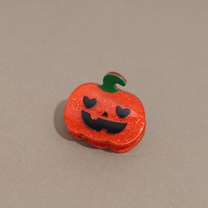 Detail of glittery orange pumpkin hair claw with heart eyes for Halloween hair styling