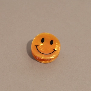 Détail d'une pince à cheveux orange vif en résine avec un motif de visage souriant
