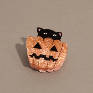 Macro detail of Halloween pumpkin hair claw with black cat and glitter acrylic finish