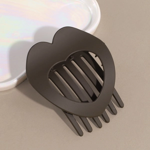 Macro shot of a matte dark brown heart-shaped hair clip on a white ceramic tray